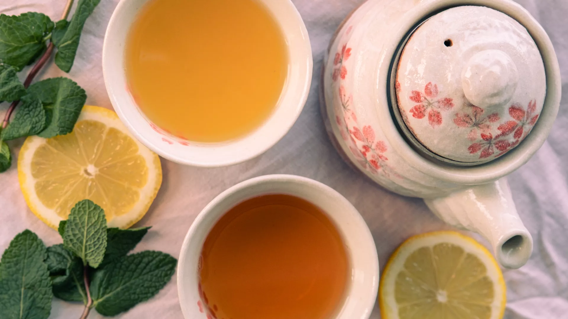 Une théière avec des tasses remplies de thés, des feuilles de menthe et des tranches de citron.